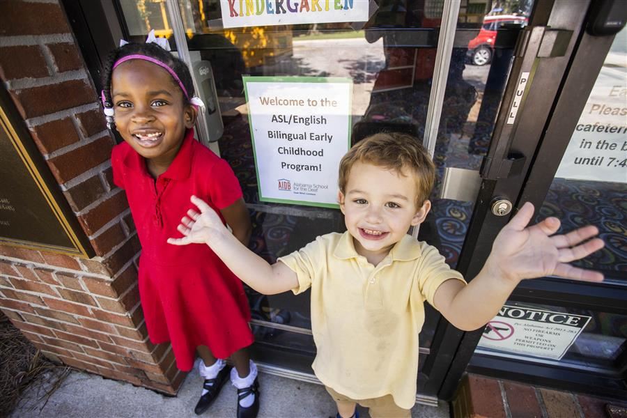 2 young children smile. A sign reads "Welcome to the ASL/English Bilingual Early Childhood Program!"